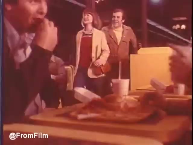 The still from the 1976 McDonald's commercial captures a lively scene inside a restaurant. Diners enjoy their meals at a table, with a group of young people entering, smiling and engaging with the atmosphere. The decor reflects the style of the era, and the food is prominently displayed, showcasing a casual and inviting dining experience. The overall vibe is cheerful and nostalgic, embodying the spirit of fast food culture in the mid-1970s.   Would you eat at McDonald's in New Orleans? Maybe…   Follow us on Twitter @FromFilm.