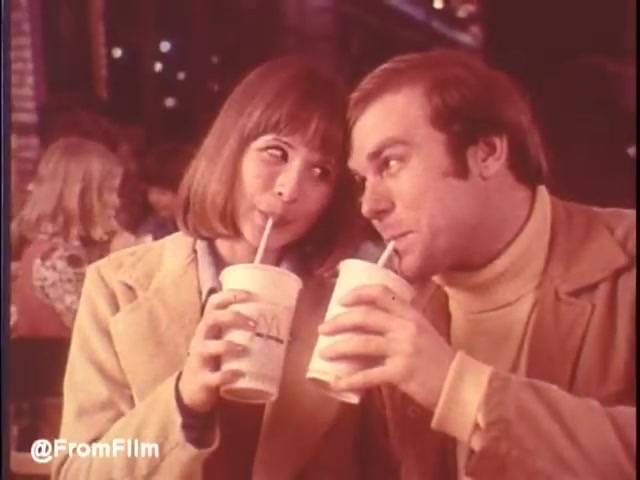 This still captures a charming moment from the 1976 McDonald's commercial set in New Orleans. A young couple, smiling and engaging, are sharing a playful drink experience with McDonald's cups in hand. The warm, vintage color palette and casual attire evoke a sense of nostalgia. The bustling background hints at a lively dining atmosphere, making McDonald's seem inviting. Would I eat at McDonald's in New Orleans? Maybe...   Follow us on Twitter @FromFilm.
