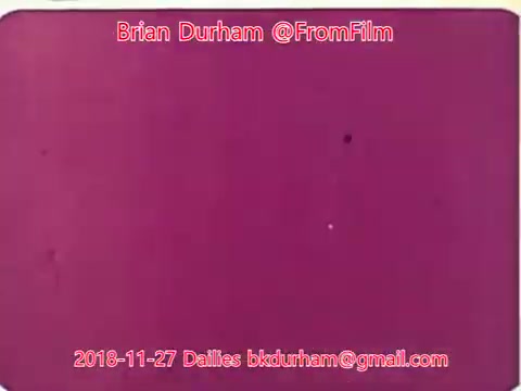 The 16mm still from '@FromFilm Dailies November 27, 2018' features a predominantly purple background with some faint spots. It displays simple visual elements typical of film dailies, possibly indicating a frame from a film in progress. Text overlays provide context, including the creator's name and contact details.