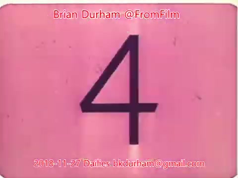 The still is a 16mm film frame showing the number '4' prominently displayed against a pink background. The image includes text indicating the creator, Brian Durham, along with the date and email address for the film dailies. The overall aesthetic is characteristic of vintage film dailies, with a simple, stylized design.