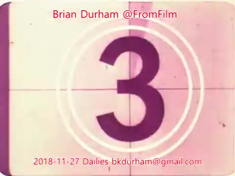 The still features a vintage film countdown, prominently displaying the number '3' in a classic circular film frame. The color palette includes faded hues, contributing to a nostalgic aesthetic typical of 16mm film. Text overlays indicate it is from Brian Durham's '@FromFilm' project, dated November 27, 2018, with a reference to 'Dailies' and an email address. The overall feel evokes a retro cinematic vibe.