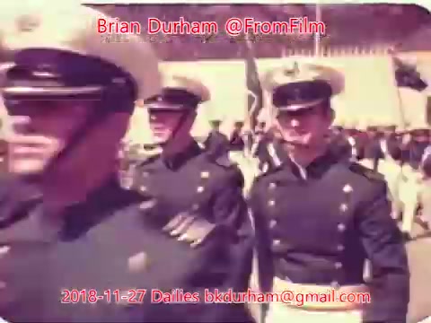 The still features a group of military personnel in formal uniforms, likely participating in a parade or ceremony. They are wearing distinctive hats and appear to be marching, showcasing a disciplined and coordinated group. The image has a vintage aesthetic, typical of 16mm film, with a slightly faded color palette. The text overlay includes the date and the creator's information.