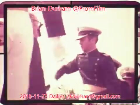 The still features a scene from a 16mm film, showcasing a military officer in uniform engaging with a civilian. The officer, identified by a cap, appears to be in a formal stance. The background is light, suggesting an outdoor setting. The image is dated November 27, 2018, and includes contact information for Brian Durham.