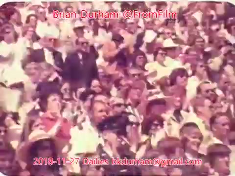 The still features a crowd of people, possibly at an outdoor event, all appearing enthusiastic or engaged. Many are dressed in light-colored clothing, and some are wearing hats. The vibrant colors suggest a lively atmosphere, typical of a celebration or gathering. The image is attributed to Brian Durham from the '@FromFilm' series, dated November 27, 2018.