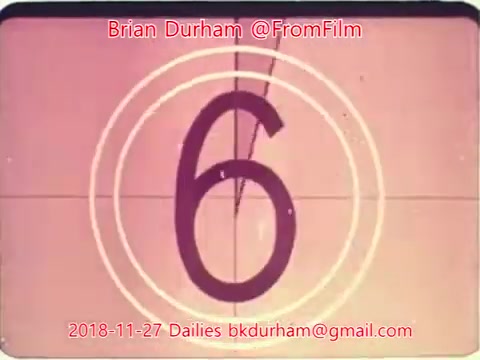 The 16mm still features a film countdown, showing the number '6' within a circular frame. The background is likely a soft color typical of vintage film. The image includes the name 'Brian Durham' and the handle '@FromFilm' prominently displayed, along with the date '2018-11-27' and a contact email at the bottom. This suggests it is a frame from film dailies, possibly indicating that filming was taking place on that date.