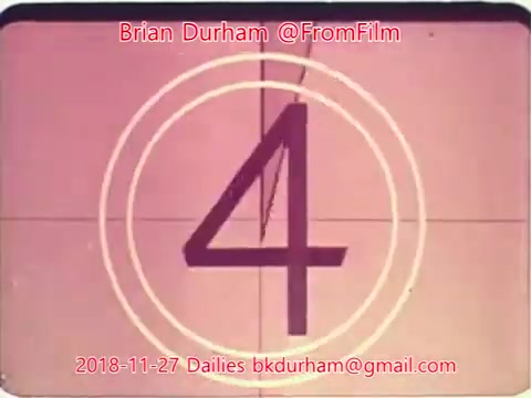 The image is a still from a 16mm film countdown, displaying the number '4' in the center. The background has a pinkish tint with a classic film countdown design, featuring concentric circles and a line at the top. Text overlays include 'Brian Durham @FromFilm' and an email address, along with the date '2018-11-27 Dailies.'