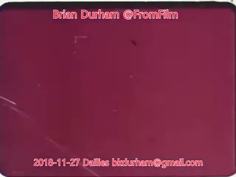 The still appears to be a frame from a 16mm film, characterized by a reddish tint and some visible scratches or imperfections typical of vintage film. It features text identifying Brian Durham and includes a date and email address. The overall aesthetic suggests an archival or experimental film context.