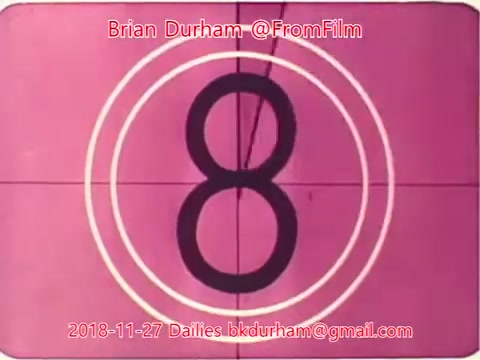 The still features a countdown timer displaying the number '8' prominently in the center. The background is a pink hue, with concentric circles surrounding the number. Text at the top includes the name 'Brian Durham' alongside the handle '@FromFilm' and the date '2018-11-27.' At the bottom, there is an email address, indicating this is part of film dailies from a 16mm film project.