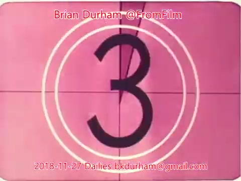 The still shows a vintage film countdown display, featuring the number '3' prominently in the center against a pink background. Circular scoring lines surround the number, typical of classic film countdowns. The image includes attribution to Brian Durham and a date of November 27, 2018, along with an email address. The overall aesthetic reflects an old-school film style.