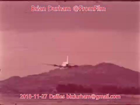 The still features an airplane landing near a mountainous backdrop. The scene is tinted with a pink hue, suggesting a sunset or dawn. Text overlays provide the creator's name, Brian Durham, and details regarding the date and context of the footage. The overall aesthetic conveys a nostalgic feel typical of 16mm film.