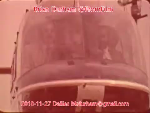 The still depicts a helicopter scene, focusing on the cockpit, which appears to show two individuals inside. The color tone is warm, suggesting a vintage effect typical of 16mm film. It’s labeled with a date, source details, and the name Brian Durham, indicating it’s part of film dailies from November 27, 2018.