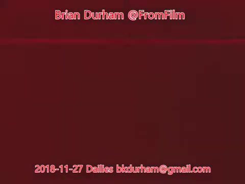 The still appears to be a red-toned image featuring text overlay that includes the name 'Brian Durham,' the handle '@FromFilm,' and a date, '2018-11-27 Dailies.' The background is a solid red, with minimal visual elements beyond the text. The overall composition suggests it's a title or frame from a film or video project, possibly indicating it's part of a daily filming log.