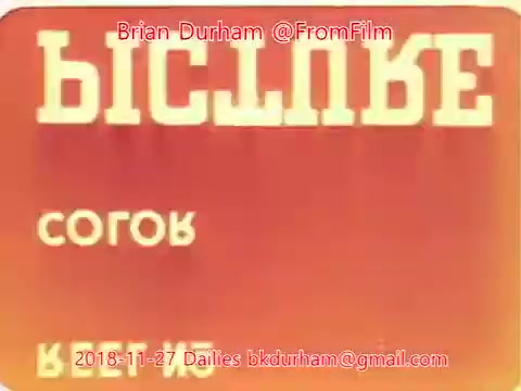 The still features a stylized text design in retro typography, predominantly using bold characters. The background is a gradient of orange, creating a warm ambiance. The text includes Cyrillic characters, suggesting it might be related to a film or media from a region using that script. The date '2018-11-27' and email address are included at the bottom, indicating it is part of a film dailies set.