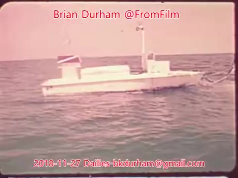 The still features a small boat floating on calm waters, likely taken during a film shoot. The color palette has a vintage quality, with soft hues typical of 16mm film. There are no discernible details about the environment or context beyond the boat itself. Text overlays indicate the source and date of the footage.