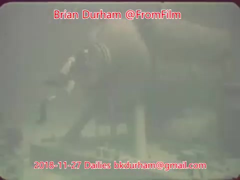 The still features an underwater scene with a person engaging with an object, surrounded by murky water and debris. The image is likely captured in low light, highlighting the mysterious and somewhat unrefined aesthetics typical of 16mm film. The text overlay includes the name Brian Durham and the date, indicating it is from film dailies.