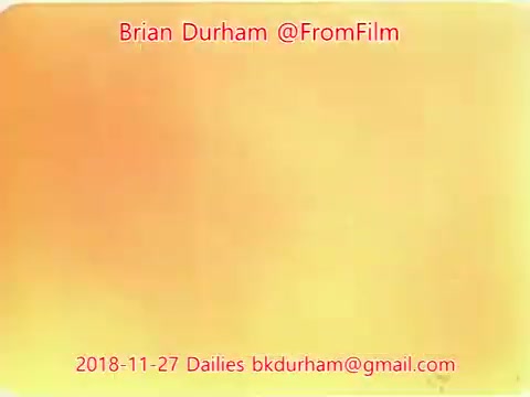 The still features a gradient of warm colors, primarily consisting of soft oranges and yellows. At the top, text indicates 'Brian Durham @FromFilm' followed by the date '2018-11-27 Dailies' and an email address. The overall aesthetic is minimalist and abstract, focusing on color rather than imagery.