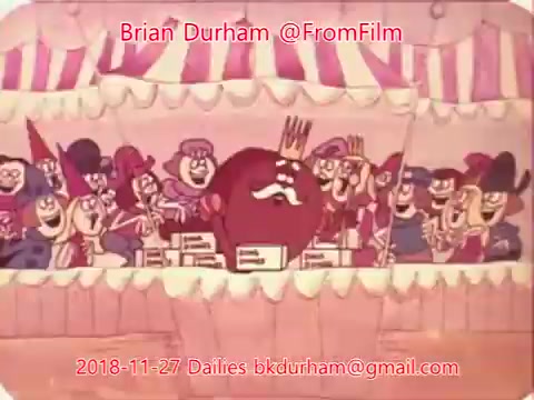 The 16mm still features a vibrant, animated scene with a large, round character at the center, likely representing a king or leader, surrounded by a colorful group of smaller characters. They appear to be in a festive setting, possibly a carnival or show, indicated by the striped canopy above. The overall mood seems joyful and lively, capturing an animation style typical of mid-20th century cartoons.