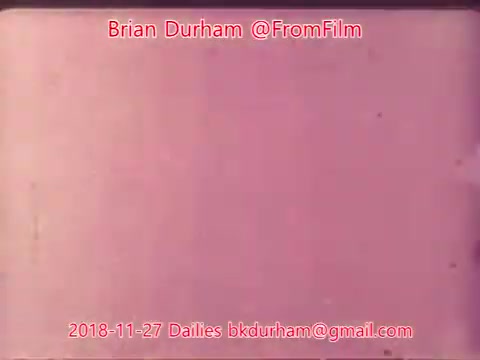 The still appears to be a 16mm film frame, showcasing a faded or tinted background that is predominantly pink. It contains text identifying the creator as Brian Durham, along with the date and contact information. The aesthetic suggests a vintage or retro style typical of film dailies from that era.