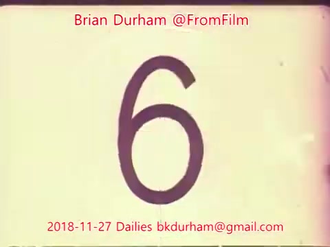 The still shows a large, bold numeral '6' on a washed-out film background, suggesting it is part of a countdown or take marker. The date '2018-11-27' and contact information for Brian Durham (@FromFilm) are overlaid in red, indicating this is from a film dailies project. The overall aesthetic reflects a vintage film look typical of 16mm footage.