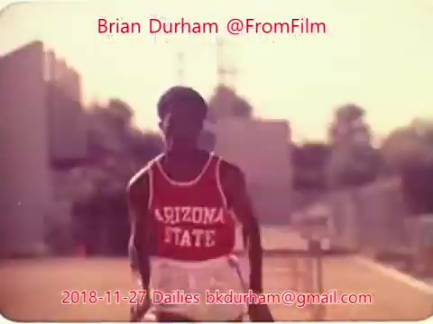 The image is a still from a 16mm film dated November 27, 2018, featuring a young athlete wearing a red and white jersey labeled 'ARIZONA STATE.' He appears to be in motion, possibly preparing to sprint, with a soft focus background that could suggest a training or competition setting. The overall color palette is warm, adding a vintage aesthetic to the scene. The image is attributed to Brian Durham and includes contact information.