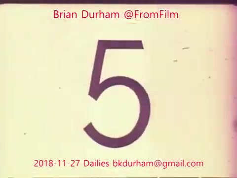 The still features a large, stylized number '5' prominently displayed in the center, likely indicating a countdown or a scene number in the context of film editing. The background appears to have a vintage film texture, typical of 16mm film, and includes the text 'Brian Durham @FromFilm' along with a date and email at the bottom. The overall aesthetic suggests it is part of a series of dailies from a film project.