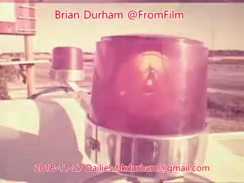 The 16mm still features a close-up of a vintage emergency light, likely from a vehicle, with a vibrant red lens and metallic base. The lighting creates a nostalgic atmosphere, typical of mid-20th-century film aesthetics. The composition suggests the image is part of a larger narrative or study related to emergency services or vehicular imagery.