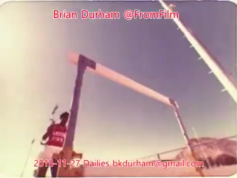 The 16mm still features a figure in a red and white outfit, likely preparing for a pole vault or similar athletic event, positioned near a vertical bar. The backdrop appears bright, possibly suggesting outdoor conditions. The image captures a moment of action or anticipation, with equipment and structures visible in the frame, indicating a sports context. The caption includes information about the creator and date, emphasizing its connection to film dailies.