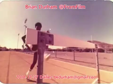The still shows a runner approaching a hurdle on a track. The scene captures the dynamic action of the athlete mid-stride, with a focus on the hurdle and the athlete's form. The colors have a vintage, muted quality, characteristic of 16mm film. Text overlays include the filmmaker's name, date, and email.