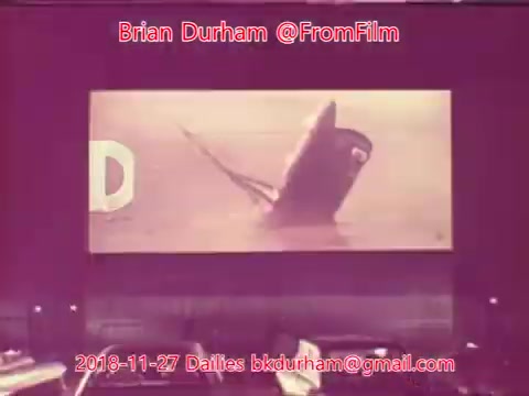 The still features a vintage 16mm film projection of a ship, possibly a rescue boat, emerging from the water. The image is partially tinted, giving it a nostalgic quality. The presence of a large letter 'D' suggests a title or branding, while the scene captures a moment of action or drama on water. The timestamp indicates it is from film dailies dated November 27, 2018.