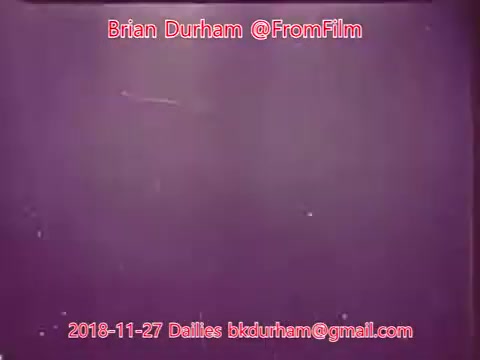 The still features a predominantly purple backdrop with noticeable scratches and imperfections typical of film dailies. Text overlays include the names 'Brian Durham,' '@FromFilm,' and an email address, indicating the source and date of the still, which is from November 27, 2018. The overall composition suggests a focus on the film's production aspects rather than a specific scene or subject matter.