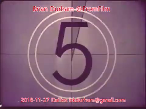 The still features a classic film countdown with the number '5' prominently displayed in a circular frame against a plain background. It has a vintage feel, typical of 16mm film aesthetics. The date, '2018-11-27,' and contact details are included, along with the username '@FromFilm' and the name 'Brian Durham.' This indicates it is part of a film dailies series.