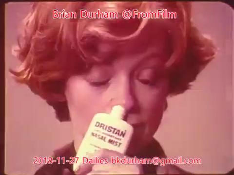 The still features a woman with short, curly reddish hair, holding a small bottle of Dristan nasal mist close to her nose. She appears to be focusing on the product, likely preparing to use it. The background is a soft color, enhancing the product's visibility. The image is part of a film daily from November 27, 2018, titled 'ffn035-dristan-dailies.'