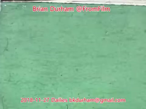 The still features a textured green wall or surface, possibly showing some wear and imperfections. The image includes text at the top and bottom identifying it as part of '@FromFilm Dailies' from November 27, 2018, along with the name Brian Durham and an email address. The overall aesthetic suggests a focus on film-like qualities, possibly indicating a raw or unedited nature.