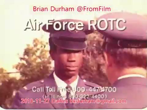 The still features a young man in an Air Force ROTC uniform, attentively listening to a senior officer. The setting appears to be an outdoor environment with trees in the background. Text overlays indicate a contact number and the date associated with the film dailies, along with the name Brian Durham. The overall tone suggests a focus on military training or recruitment.