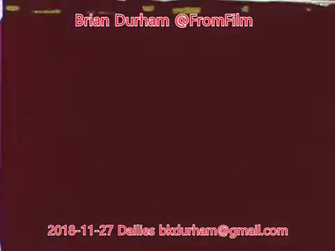The 16mm still features a reddish, textured background with minimal detail. It includes credits for 'Brian Durham @FromFilm' and metadata indicating the date, '2018-11-27,' along with a contact email. The overall aesthetic suggests a raw or unfinished quality typical of film dailies.