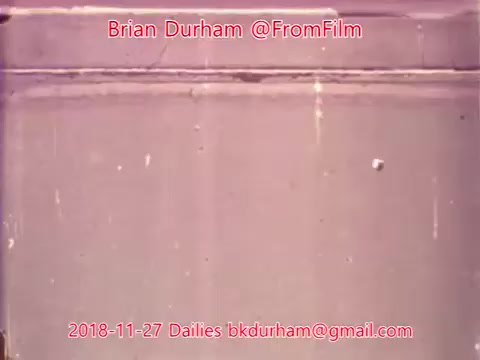The still features a textured surface, likely a wall or backdrop, with a faded color tone typical of 16mm film. There are faint marks or imperfections visible, characteristic of film dailies. The text overlay includes the name 'Brian Durham,' the handle '@FromFilm,' the date '2018-11-27,' and an email address, indicating it’s part of a series of film dailies.