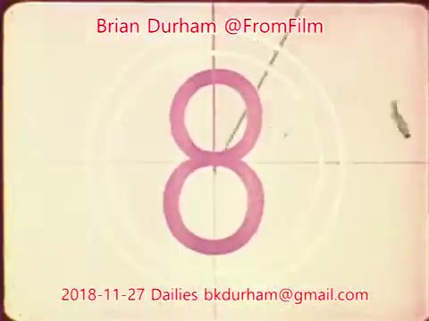 The still features a vintage 16mm film countdown displaying the number '8' in a pink circle. The background shows a film frame with concentric circles typical of old film projectors. Text overlays indicate the creator, Brian Durham, and the date of the dailies, November 27, 2018, along with contact information. The overall aesthetic reflects a retro film style.
