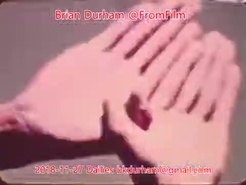 The still features two hands positioned closely together, possibly in a gesture of showing something small. The image has a soft, vintage quality typical of 16mm film, with warm hues. There are overlaid text details indicating the source and date, suggesting it is part of film dailies from November 27, 2018.