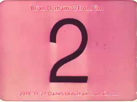 The still features a large, stylized number '2' against a soft pink background. The image bears marks of film, typical of 16mm projection, and includes timestamps and identifiers such as 'Brian Durham @FromFilm' and '2018-11-27 Dailies.' The overall aesthetic suggests a vintage or classic film style.