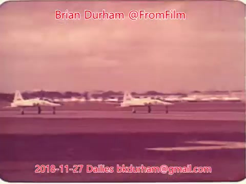The still appears to show a pair of aircraft, likely military jets, taxiing on an airfield. The scene features a hazy, vintage aesthetic typical of 16mm film, with a muted color palette. In the background, more aircraft can be seen, indicating an active airfield environment. The date and credits suggest it is part of a series of film dailies from November 27, 2018, attributed to Brian Durham.