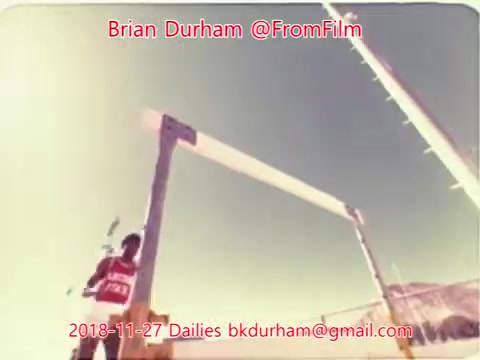 The still features a skier preparing to take off from a ramp, with a clear blue sky in the background. The skier is wearing a red outfit and appears focused, suggesting an action or competitive scene. The image conveys a sense of anticipation, likely from a skiing event captured on 16mm film.