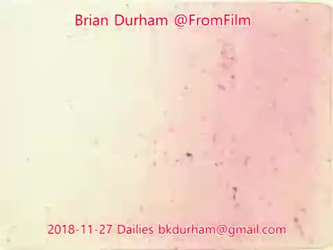 The still features a faded, abstract background with a gradient transitioning from light cream to soft pink, speckled with dirt and scratches typical of aged film. The text overlay includes the name 'Brian Durham,' the handle '@FromFilm,' and the date '2018-11-27 Dailies,' suggesting it is part of a film project or archive. The overall aesthetic evokes a nostalgic, vintage feel.