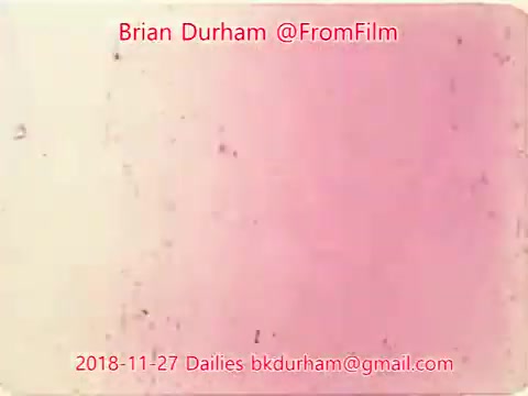 The 16mm still from '@FromFilm Dailies November 27, 2018' features a faded, pinkish background with a few specks and marks, suggesting an aged or distressed film look. Text overlays include the name 'Brian Durham,' the handle '@FromFilm,' and a date reference, along with an email address for contact. The overall tone is nostalgic and reflective of classic film aesthetics.