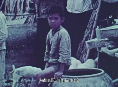 The still features a young boy sitting beside a large pot in a rural setting, likely representing the struggles faced by children in underprivileged circumstances. The muted colors and worn clothing highlight themes of poverty and need, characteristic of Save the Children's messaging in their 1968 PSA. Surrounding elements suggest a simple, perhaps challenging lifestyle, emphasizing the organization's mission to assist vulnerable children.