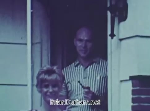 The still from the 1968 'Save The Children' PSA features a man and a woman standing in a doorway. The woman has light, curly hair and appears cheerful, while the man, wearing a striped shirt, is holding a pipe. The scene conveys a sense of warmth and community engagement, typical of public service announcements promoting charitable efforts.