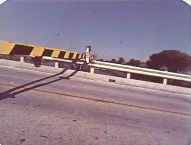 The still from the trailer for 'Double Bill: 'Dirty Mary, Crazy Larry' and 'Vanishing Point'' features a close-up of a road barrier, marked with black and yellow stripes, set against a clear blue sky. The scene appears to evoke a sense of tension or anticipation, typical of automotive thrillers. The trailer likely presents elements from both films, emphasizing themes of high-speed chases and adventure. The vintage quality of the 16mm film captures the essence of classic cinema.