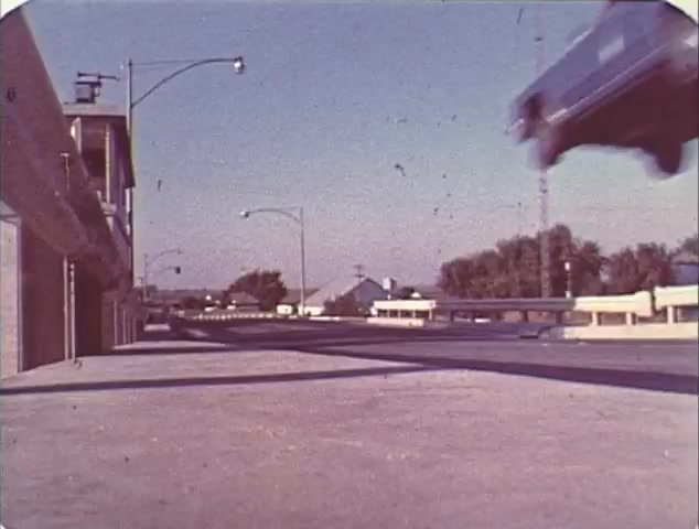 The still from the 'Double Bill: 'Dirty Mary, Crazy Larry' and 'Vanishing Point'' trailer features a car in mid-air, capturing a dynamic action scene typical of 1970s car chase films. The setting appears to be an urban area with clear skies, showing a mix of road infrastructure. This moment emphasizes the thrill and excitement of the films being showcased. The visual quality reflects the era's filmmaking style, characteristic of reissue trailers aimed at nostalgia.