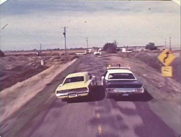 The still from the 'Double Bill: 'Dirty Mary, Crazy Larry' and 'Vanishing Point'' TV spot trailer depicts a tense car chase scene. The image shows a yellow car closely racing alongside a police vehicle on a rural road. The background features open fields and a clear sky, emphasizing the high-speed pursuit. This moment captures the essence of 1970s car chase films, highlighting themes of rebellion and adrenaline typical of both featured movies. The overall aesthetic reflects the retro style of 16mm film, adding to its nostalgic appeal.