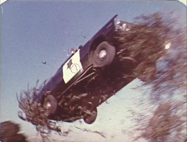 The still depicts a dramatic moment from a 16mm trailer for the double bill of 'Dirty Mary, Crazy Larry' and 'Vanishing Point.' It shows a car, likely a police vehicle given the markings, soaring through the air over a landscape, surrounded by brush. The scene emphasizes action and excitement, key elements in both films. This reissue trailer captures the essence of the car chase genre that characterized these classics, showcasing thrills and high-energy sequences.
