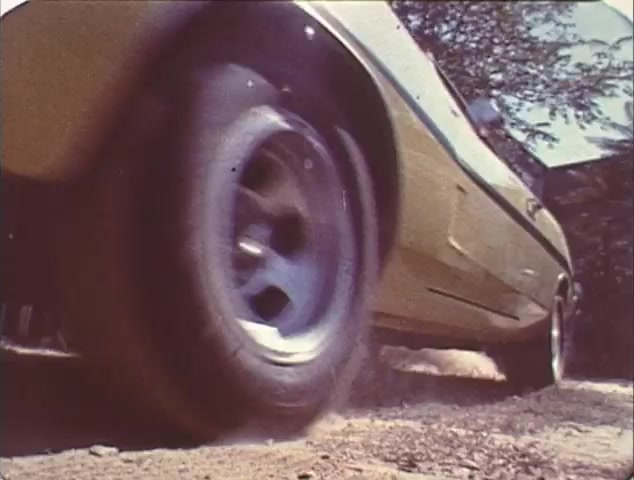The still from the 'Double Bill: 'Dirty Mary, Crazy Larry' and 'Vanishing Point'' TV spot trailer features a close-up of a tire on a yellow car, kicking up dust on a dirt road. This emphasizes the high-speed action typical of both films. The shot likely captures the intensity and thrill of car racing and chase scenes, which are prominent themes in these movies. The gritty texture and grain of the 16mm film highlight its vintage appeal, making it a nostalgic glimpse into classic cinema trailers.